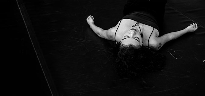 Mulher de cabelo cacheado e vestido escuro deitada no chão, foto em preto e branco
