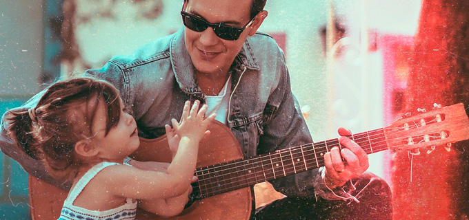 Músico Dan Arruda tocando violão enquanto sua filhinha bate palma ao seu lado