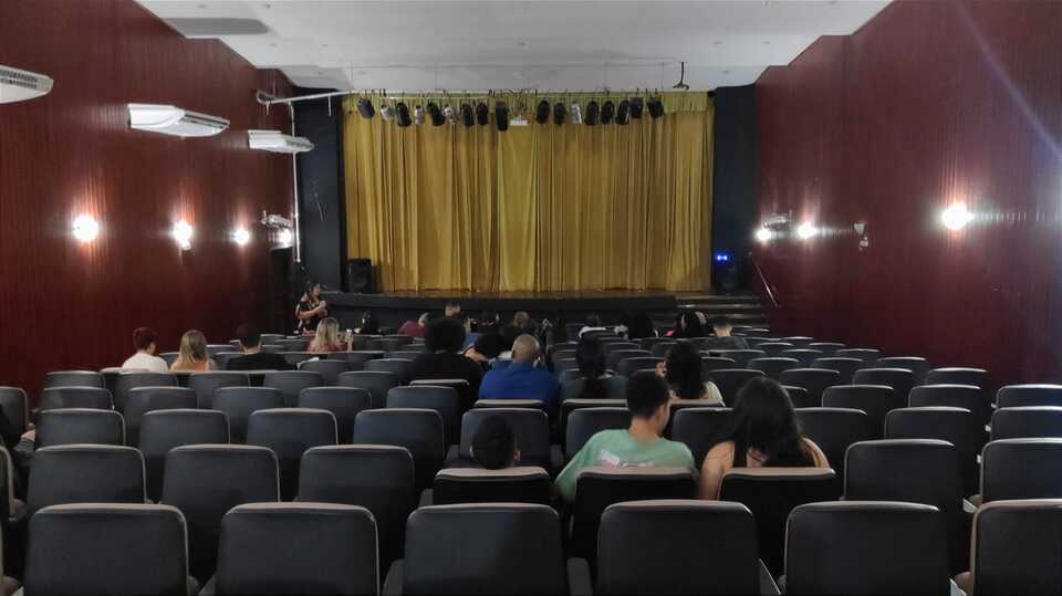 teatro com poucas pessoas e a cortina do palco fechada
